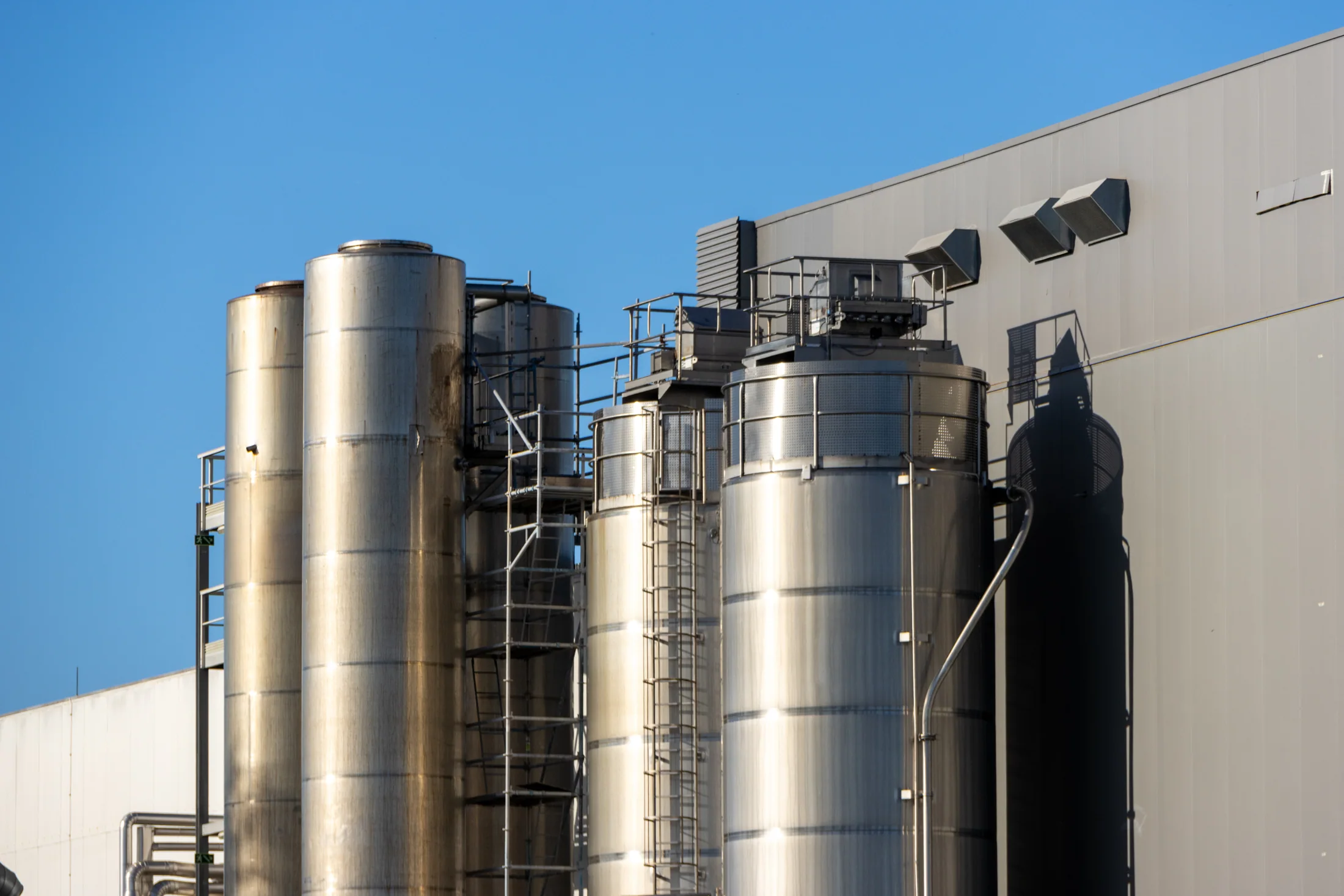 Stainless steel ingredient silos beside a food processing building under a blue sky.