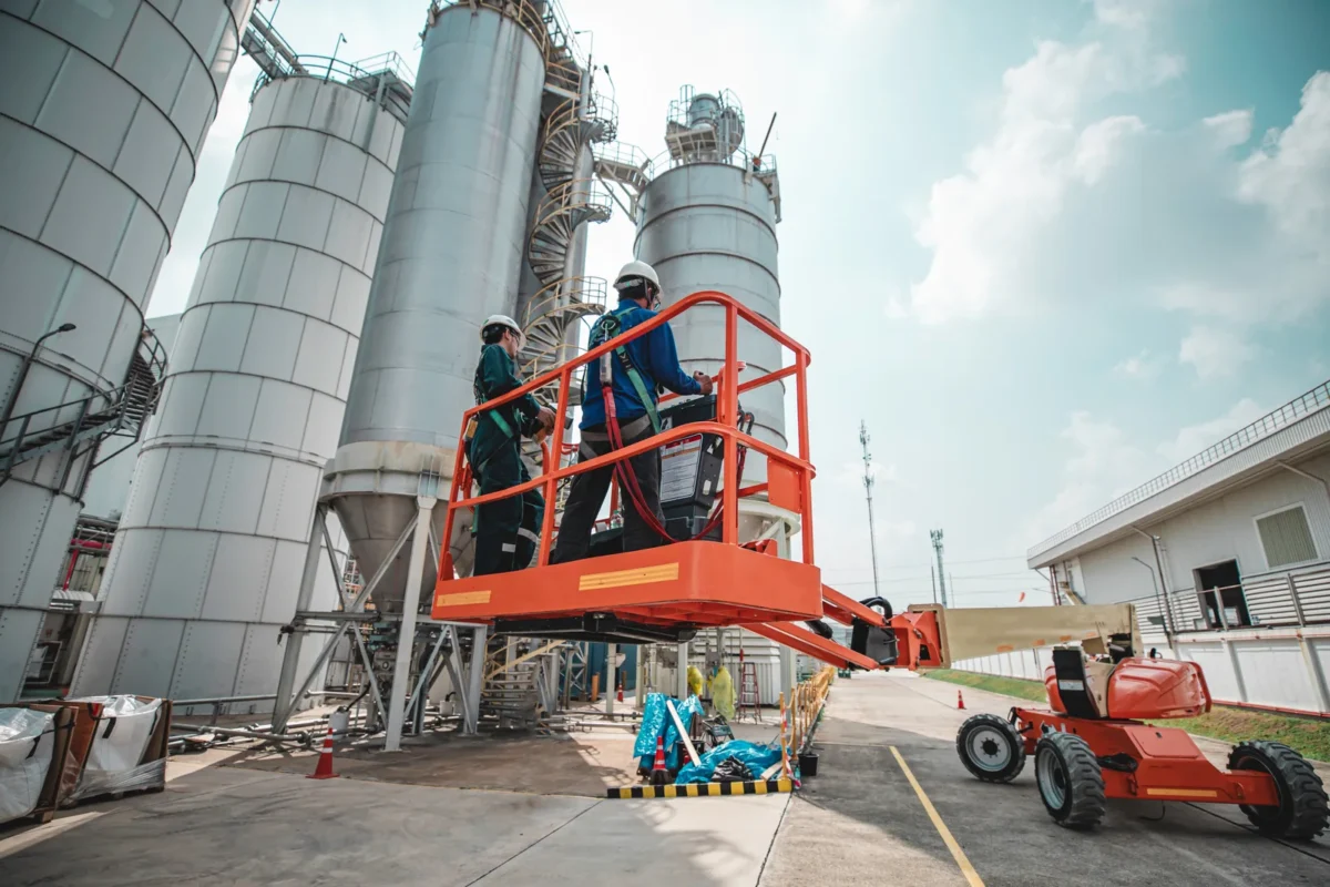 Industrial workers on a raised access platform beside tall storage silos.