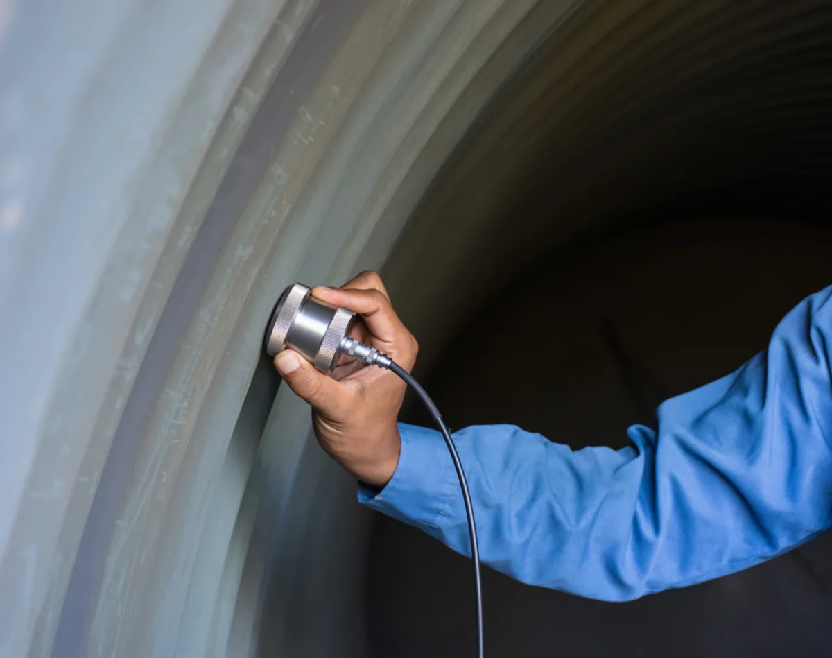 Technician applying an ultrasonic inspection probe to a curved metal vessel wall.